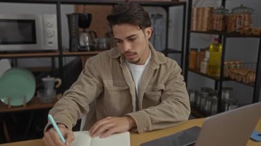 Ofisteki İspanyol bir adam, mutfak eşyaları ve not defteriyle süslenmiş bir odada dizüstü bilgisayarla oturup iş ortamındaki stresi gösteren bir yazı yazarken endişeli görünüyor..