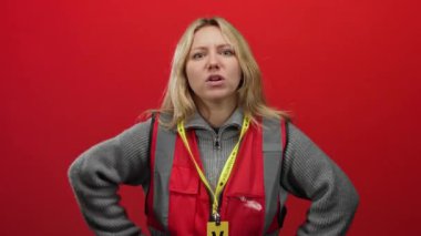 Genç bir kadın, canlı kırmızı bir duvarın önünde, gri bir süveter ve kırmızı bir yelek giyerek büyük bir tutkuyla jest yaparken yoğun duygular sergileyerek hayal kırıklığını ifade ediyor..