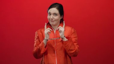 Kırmızı arka planda turuncu tulum ve kelepçe takan kadın çeşitli duygular ifade ediyor. Hapis ve adalet kavramını gözler önüne seriyor..