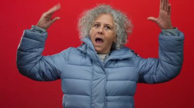 İnzivaya çekilmiş kırmızı bir zemine karşı enerjik bir şekilde el kol hareketi yapan mavi bir kış ceketi giyen, canlı sahnelerde güçlü duygular taşıyan bir kadın..