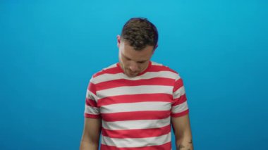 Parlak mavi duvara karşı çizgili gömlekli genç adam rahat ve düşünceli görünüyor. Kafası eğik, rahat ve dışa dönük bir tavır sergiliyor.