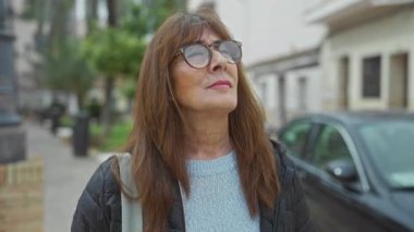 Şehir sokaklarında gülümseyen gözlüklü yaşlı İspanyol kadın şehir hayatı ve çevre koşullarından zevk alırken yüzündeki memnuniyet ve sükuneti gösteriyor.