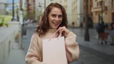 Elinde alışveriş çantası olan genç bir kadın şehir dışında süveter giyiyor. Heyecan verici. Kadın yaşam tarzı eğlence alışverişi yapıyor..