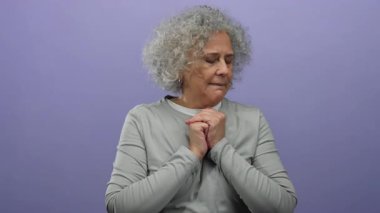 Mor arka planda duran gri saçlı kadın düşünceli ve dalgın görünüyor, orta yaşlı ve olgun olmanın zarafet ve bilgeliğini somutlaştırıyor..