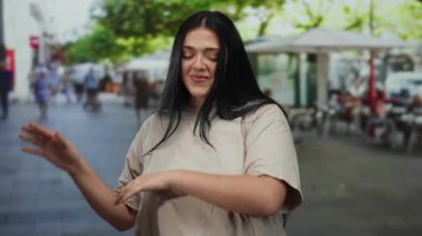 Genç ve cüsseli bir kadın açık hava kafeleri ve ağaçlarla dolu bir caddede neşeyle dans ediyor kıvrımlı güzelliğini hareketli bir şehir ortamında sergiliyor..