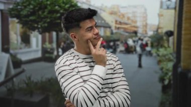 Şehir sokaklarında düşünceli bir ifadeyle gezen, çizgili süveter giyen, bulanık şehir geçmişi olan, düşüncelere dalan ve hareketli bir ortamda günlük tarzını sergileyen bir adam..