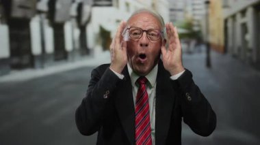 Takım elbiseli kıdemli bir adam açık hava ortamında elleri havada gülüyor, iş başarısını ve mutluluğu resmediyor..