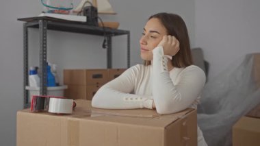 Yeni evdeki paketlenmiş kutuların yanında gülümseyen kadın, hareket sırasında heyecan ve beklentiyi yansıtıyor.