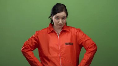 Turuncu hapishane tulumlu kadın yeşil arka planda duruyor. Kendine güvenen ifadeyle, iki eliyle aşağıya bakıyor. Hapis kavramını canlı bir şekilde temsil ediyor..