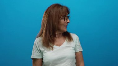 Neşeli bir ifade ve günlük bir stil sergileyen, izole bir ortamda canlı mavi bir arka plana heyecanlı bir şekilde gülümseyen ve işaret eden bir kadın..