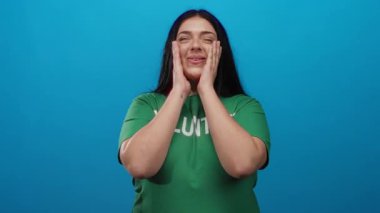 Gönüllü kadın yeşil gömleğiyle, canlı mavi arka plana karşı gülümsüyor. Toplumun ruhunu ve neşeli ifadesini sergiliyor.