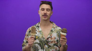 Genç İspanyol adam canlı mor arka planda dondurmayı seviyor. Tropikal gömlek ve güneş gözlüğü takıyor. Neşeli bir turist havası var..