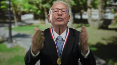 Takım elbiseli kıdemli bir adam açık hava parkında neşe içinde olumlu duygular ifade ediyor..