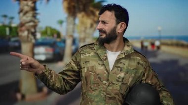 Askeri üniformalı İspanyol bir adam, güneşli bir caddede arka planda palmiye ağaçları olan ve yönünü ve amacını bildiren açık havayı işaret ediyor..