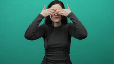 Gözleri kaplayan esmer bir kadın yeşil arka planda şaşırmış, etkileyici duygular sergiliyor..