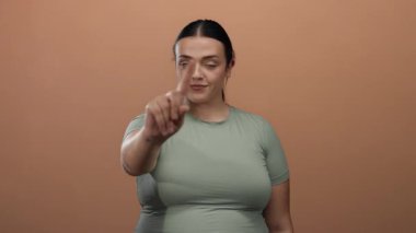 Hayır diyen bir kadın, kahverengi bir arka planda, kendine güvenen genç ve iri yarı bir kadının ifadesini izole bir ortamda yakalıyor..