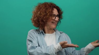 Orta yaşlı, kıvırcık saçlı, neşeli yeşil bir arka plana karşı elleri açık el hareketleriyle gülümseyen İspanyol bir kadın. Dostça bir hava sergiliyor..