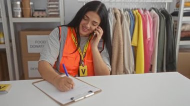 Siyah saçlı, turuncu yelekli gönüllü bir kadın. Telefonla konuşuyor. Bağış merkezinde..