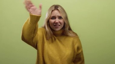 Sarı süveter giymiş, yeşil arka planda bağıran, güçlü duyguları vurgulayan ve neşeli iletişim için izole edilmiş jestleri olan bir kadın..