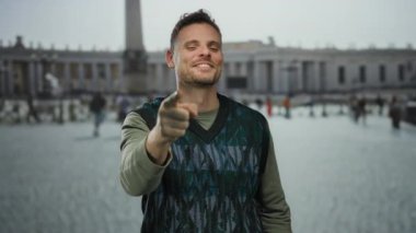 Kentsel Vatikan 'da gülümseyen ve kameraya bakan genç bir adam. Arka planda güneşli gökyüzünün altında bulanık insanlar var..