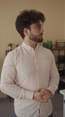 Ofiste sakallı, gözlüklü ve pembe tişörtlü, bitkilerle ve kitaplarla çevrili genç bir adam, profesyonel ve düşünceli bir davranış sergiliyor..