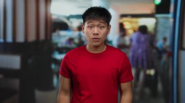 Kırmızı gömlekli genç adam hareketli bir otel ortamında coşkulu bir şekilde el kol hareketi yapıyor, sahneye enerji ve canlılık katıyor, hareketli ve çekici bir atmosfer yaratıyor..