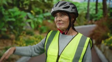Parktaki yaşlı İspanyol kadın, kaskı ve güvenlik yeleği giyip doğal ortamdaki doğal aktiviteler sırasında tuhaf bir ifadeyle etrafa bakıyor..
