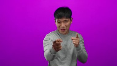 Genç adam parlak pembe bir arkaplanı işaret ediyor ve gülümsüyor, günlük gri bir gömlek giyiyor, stüdyo ortamında izole edilmiş, pozitiflik ve nişan iletiyor..