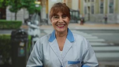 Kıdemli İspanyol kadın açık havada üniformalı bir şehir caddesinde gülümsüyor, açık havada çalışkan bir bağlılığın özünü yakalıyor..