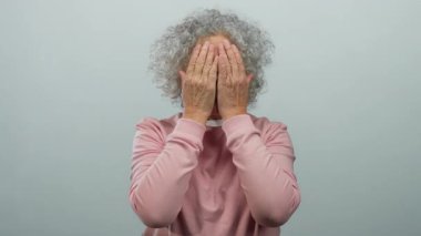 Beyaz tenli arka planda gülümseyen ve yüzünü gösteren gri saçlı yaşlı bir kadın..