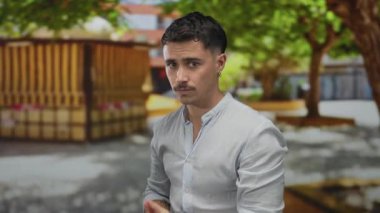 Ağaçlarla çevrili güneşli bir parkta el kol hareketleriyle silah taklit eden genç bir İspanyol.