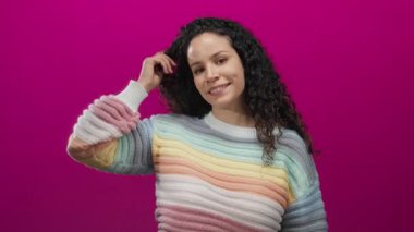 Canlı pembe arka planda gülümseyen, renkli süveter giyen neşeli bir kadın..