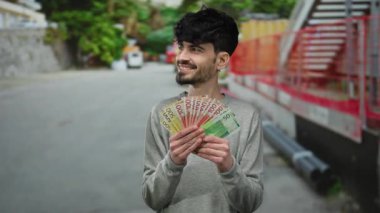 Norveçli kronu elinde tutan adam şehir sokaklarında çeşitli duygular ifade ederek para ve modern yaşam tarzını gözler önüne seriyor..