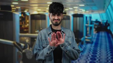 Spor salonunda hoşlanmadığını ifade eden genç bir adam, kot ceket giyiyor, modern fitness ekipmanlarının arka planına karşı..