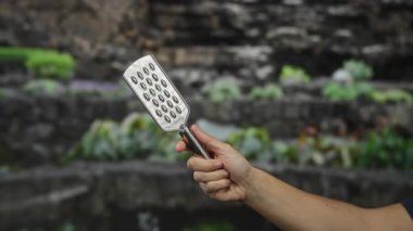 Yeşillik yemyeşil, açık havada basit yemek pişirme aletleri sergileyen bir adam, erkek elini doğal arka plana karşı vurguluyor..