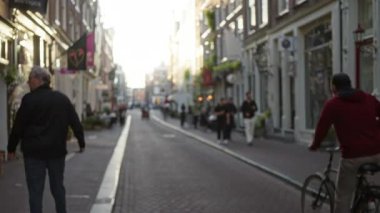 Avrupai bir şehirde yürüyen ve bisiklete binen bulanık insanların olduğu sokak sahnesi, gün ışığında bokeh etkisini ve canlı şehir atmosferini yakalıyor..