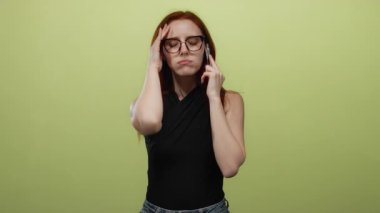 Gözlüklü ve kızıl saçlı bir kadın, sarı bir duvara karşı hayal kırıklığı ve kafa karışıklığı gösteriyor. Duyguları ve iletişim mücadelesini vurgulayan üç duygusal kareden oluşan bir dizi..