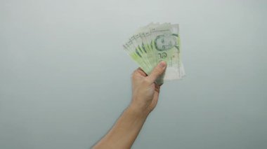 Beyaz duvar zeminine karşı Singapur dolarları tutan adam, para ve finans kavramını gözler önüne seriyor ve erkekler tarafından izole edilmiş banknotlar kullanıyor..