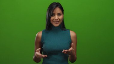 Yeşil duvarın karşısında gülümseyen, elleri titreyen, dinamik ve canlı bir ifade yakalayan, yeşil bluzlu bir kadın..