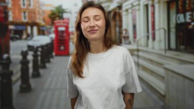 Kadın hareketli bir şehir caddesinde arka planda ikonik kırmızı telefon kulübesi ile neşeli bir şekilde gülüyor açık hava atmosferini yakalıyor..
