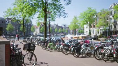 Bulanık bisikletler Amsterdam 'da güneşli bir günde canlı ağaçların altında yürüyen insanlarla dolu bir kanal oluşturur..