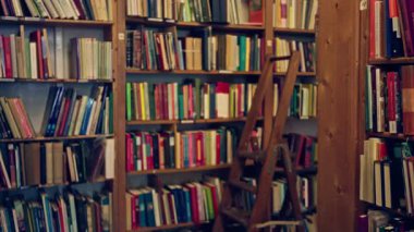 Renkli kitaplarla dolu kütüphane rafları ve ahşap bir merdiven eğitim ve bilgi odaklı davetkar ve samimi bir okuma ortamı yaratıyor..