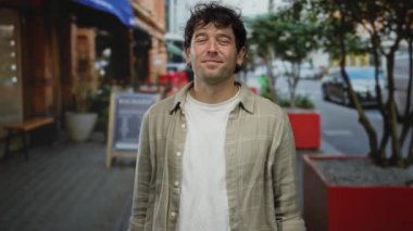 İspanyol bir adam restoran terasında kollarını kavuşturmuş gülümsüyor, canlı bir sokak geçmişine karşı kurulmuş, şehir hayatını ve günlük zarafeti çağrıştırıyor..