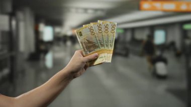 Norveç Kronu 'nu elinde tutan adam, yoğun bir terminal ortamında seyahat ve finansmanı ön plana çıkarıyor..