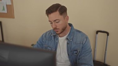 Sakallı genç adam sessiz duruyor ve ofis masasında kulaklarını kapatıyor..