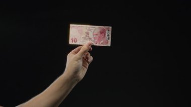 Elinde Türk lirası banknotları tutan adam siyah arka planda izole edilmiş, minimalist bir ortamda para birimine odaklanıyor..