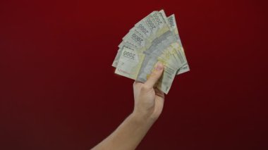 Endonezya rupia banknotları tutan adam canlı kırmızı bir arka plana karşı.