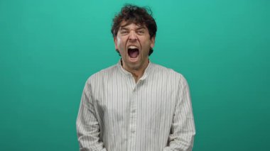 Yakışıklı İspanyol bir adam canlı yeşil bir arka plana karşı ifade ile bağırıyor, çizgili bir gömlek giyiyor, yakın plan bir portrede yoğun duygular taşıyor..