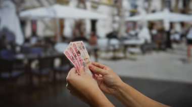 Kirli paraları tutan eller, arka planda bulanıklık olan kalabalık bir kahve dükkanının terasında..