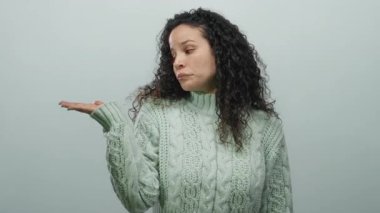 Yeşil kazaklı bir kadın, kollarını aralayıp beyaz arka planda izole edilmiş bir şekilde omuz silkiyor. Stüdyoda belirsizlik duygusunu gündelik tarzda ve İspanyol kökenli bir şekilde aktarıyor.